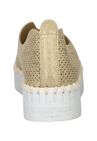 Zapato slip-on de punto beige con una parte superior texturizada, parte trasera elasticada y suela de goma blanca con costuras y una marca en el talón.