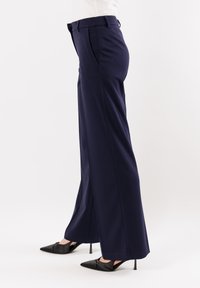 Pantaloni larghi blu navy realizzati in tessuto testurizzato, con vita alta, tasche laterali e una vestibilità rilassata, abbinati a tacchi alti neri.