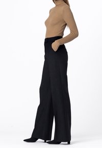 Bruine geribbelde coltrui en zwarte wijde broek met hoge taille. De broek heeft zijzakken en een slank design.