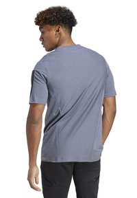 Maglietta sportiva grigia con maniche corte, tessuto testurizzato, cuciture rinforzate e linee di design sottili, indossata con pantaloni sportivi neri.