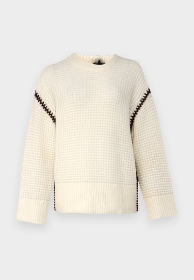 Pull crème avec un motif texturé, doté de coutures d'accent marron le long des épaules et des fentes sur les côtés. Manches longues, col rond.