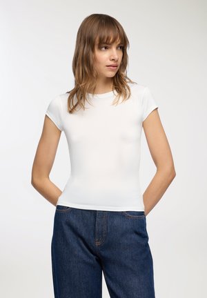 T-shirt bianco a maniche corte con scollatura rotonda e una texture liscia e aderente, abbinato a jeans in denim blu scuro a taglio dritto.