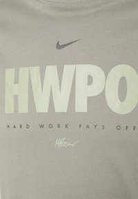 Camiseta de algodón gris con un gran texto en verde claro que dice "HWPO" y "HARD WORK PAYS OFF" debajo. Incluye un pequeño logo de Nike y un detalle de firma.