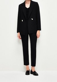 Černý elegantní blazer s dvěma velkými knoflíky, spárovaný s úzce střiženými černými kalhotami a černými loafers. Čisté linie a strukturovaný design.