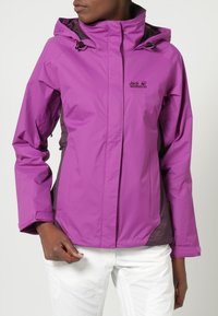 Chaqueta impermeable morada con capucha, que presenta un logotipo negro, acentos oscuros contrastantes y un diseño elegante y ligero.