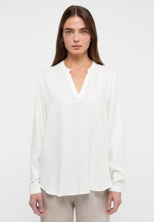 Blusa bianca a maniche lunghe con scollatura a V, realizzata in tessuto morbido; presenta un orlo arrotondato e dettagli di cucitura sottili.