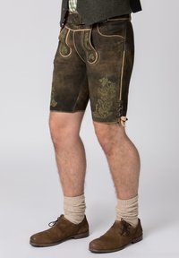 Traditionele bruine leren shorts met groene bloembroderie, contrasterende stiksels en zijkantveters, gecombineerd met bruin schoeisel en crèmekleurige sokken.