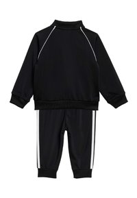 Μαύρο σετ φόρμας με ζακέτα με φερμουάρ και ψηλό γιακά, διακοσμημένη με λευκές ρίγες στο πλάι, συνδυασμένη με αντίστοιχο παντελόνι με στενή γραμμή.