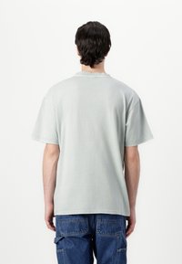 Lichtgroene katoenen t-shirt met korte mouwen, een ronde hals en een relaxte pasvorm. Gepersonaliseerde afwerking met zichtbare stiksels.