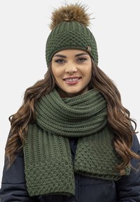 Bonnet tricoté vert avec un pompon et une écharpe assortie avec des motifs texturés. Les deux sont fabriqués en laine épaisse et chaude pour un port d'hiver.