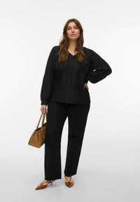 Blouse noire texturée avec un col en V, associée à un pantalon noir à jambes droites. Sac à main marron et chaussures marron à bout pointu complètent la tenue.