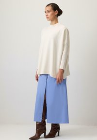 Krēmas krāsas adīta džemperis ar ribu detaļām, saskaņots ar gaiši zilu midi svārku ar priekšējiem pogu aizvēršanas elementiem. Brūni augstpapēžu zābaki līdz ceļgaliem.