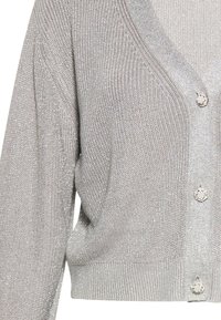 Cardigan gri deschis cu decolteu în V, textură striată și butoane decorative. Fabricat dintr-un tricot moale cu un finisaj ușor strălucitor.