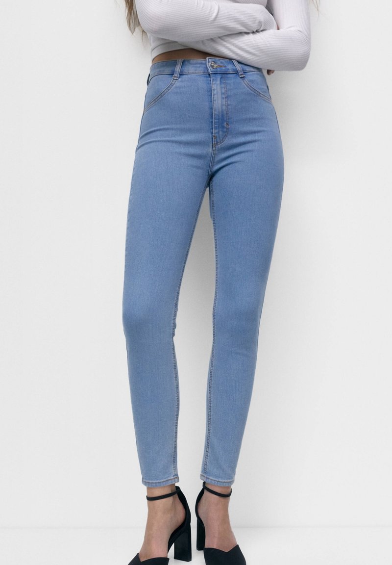 Jean skinny taille haute bleu clair en denim, présentant un design classique à cinq poches et des détails de couture subtils.