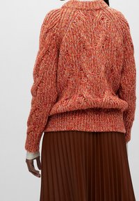 Strickpullover in roten und orangefarbenen Nuancen, ausgestattet mit einem gerippten Kragen und Saum, in lässiger Passform und mit Kabelstrickmuster.