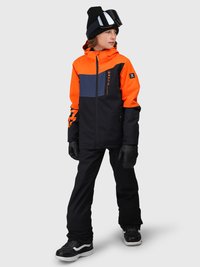 Bambino che indossa un giubbotto invernale arancione, nero e grigio, pantaloni da neve neri, guanti neri, berretto nero e occhiali protettivi, in piedi e che guarda a destra.