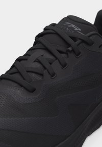 Κοντινό πλάνο μαύρου αθλητικού παπουτσιού με κορδόνια, που δείχνει υφή υφάσματος, λείες επικαλύψεις και μέρος της ενισχυμένης σόλας.