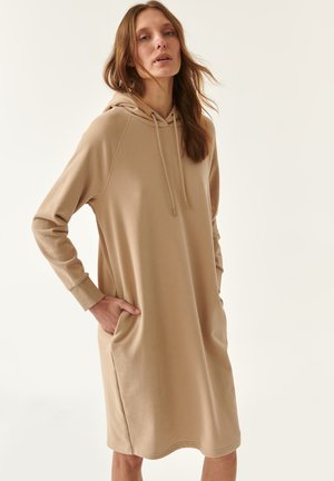 Robe à capuche beige en tissu doux, longueur genou avec une coupe décontractée, poches latérales et cordon de serrage à capuche. Manches longues avec bords côtelés.