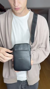 Črna usnjena torba za čez ramo z dvema zadrgo zaprtima predeloma, okrašena s šivanjem in z odstranljivim trakom, ki ima sponko. Prikazan je logotip "VALENTINO".