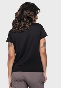 Schwarzes T-Shirt mit kurzen Ärmeln, rundem Halsausschnitt und glatter Textur. Sichtbare Tattoos am linken Arm. Aussehen in einfarbig ohne Muster.
