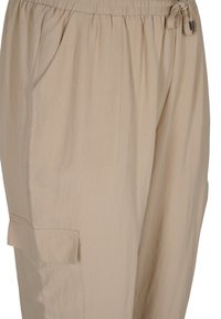 Béžové volné kalhoty s elastickým pasem, šňůrkou a bočními kapsami; vyrobené z lehkého materiálu s hladkou texturou.
