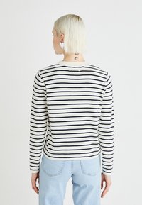 Stripet genser i myk stoff, med marineblå striper på en off-white bakgrunn, rund halslinning og lange ermer.