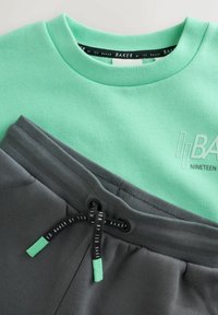 Mintgroene trui met ronde hals en gestructureerd logo; gecombineerd met donkergrijze shorts met een trekkoord en contrasterende groene uiteinden.