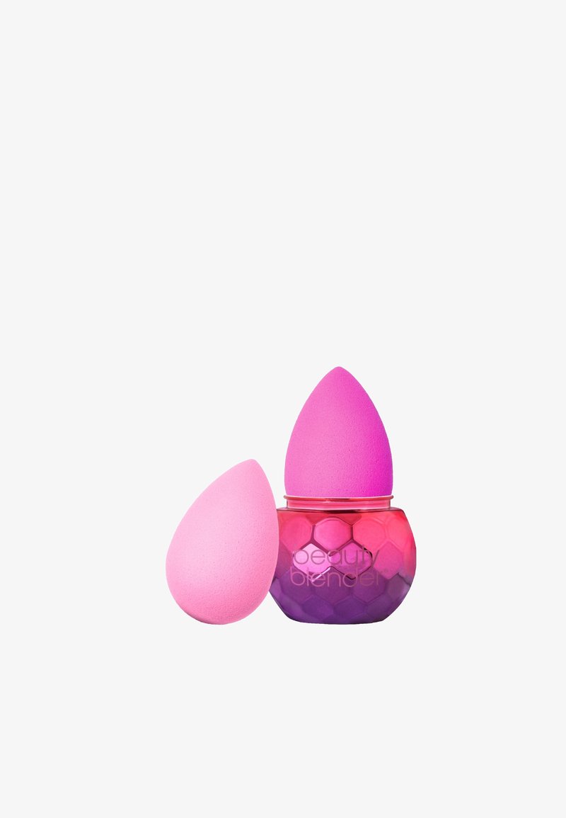 Roze make-up sponsen in een druppelvorm, één in een honingraat-achtige container die overgaat van roze naar paars, met een gouden rand.