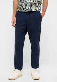 Granatowe bawełniane spodnie o luźnym kroju, z bocznymi kieszeniami i elastycznymi mankietami, w połączeniu z białymi sneakersami.