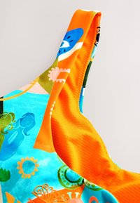 Bretea colorată pentru costum de baie, cu un model vibrant albastru și portocaliu, cu forme abstracte. Confecționată dintr-un material neted și elastic.