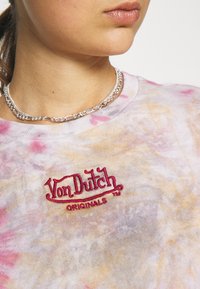 Pastelinė spalvų marmurinė marškinė su rausvais, geltonais ir violetiniais raštais; priekyje yra siuvinėtas logotipas „Von Dutch ORIGINALS“. 
