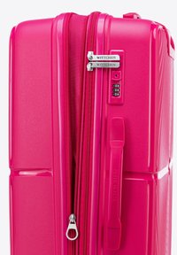 Maleta rígida de color rosa brillante que presenta dobles cremalleras, una cerradura de combinación y una superficie texturizada con elementos de diseño en relieve.