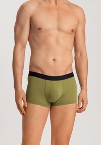 Boxers de color verde oliva hechos de tela suave con una cinturilla elástica negra que presenta el nombre de la marca. Diseño ajustado con cobertura moderada.