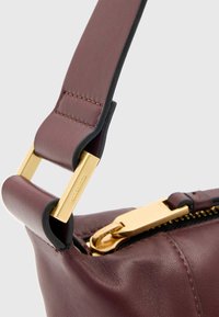 Bordeauxrode leren handtas met accenten van goudkleurige hardware. Heeft een gestructureerd oppervlak, een ritssluiting en een brede band met een contrasterende rand.