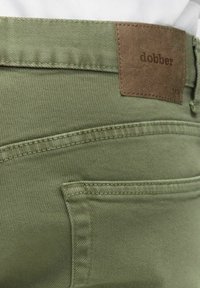 Gröna bomullstwillbyxor med en brun läderetikett som har texten "dobber." Funktioner inkluderar slim fit, sydda fickor och en knappknäppning.