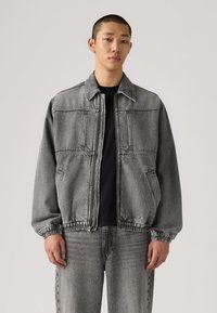 Τζιν μπουφάν σε γκρι, με φερμουάρ μπροστά, δύο μπροστινές τσέπες και ελαστικές μανσέτες. Σετ με τζιν παντελόνι στο ίδιο γκρι χρώμα.