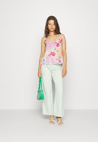 Camisola com estampado floral em azul claro, com flores rosa e amarelas; combinada com calças largas verde claro e sandálias brancas de tiras. Bolsa verde.