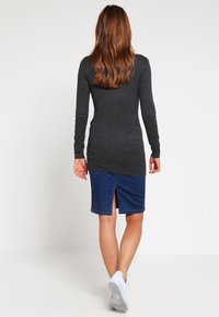 Szary top z długim rękawem połączony z niebieską spódnicą z denimu z rozcięciem z tyłu. Strój uzupełniają białe trampki.