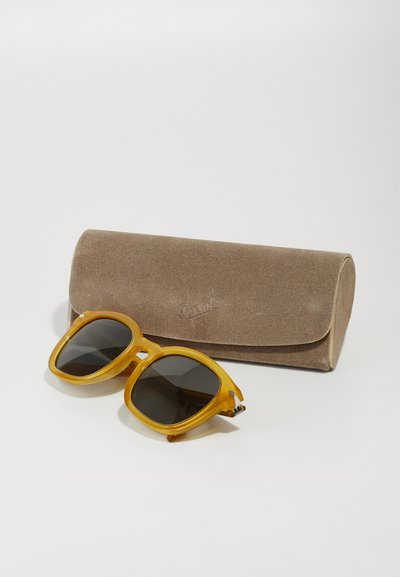 Óculos de sol de acrílico amarelo com lentes escuras, apresentando um formato quadrado e robusto. Acompanham uma estojo macio de camurça castanha.