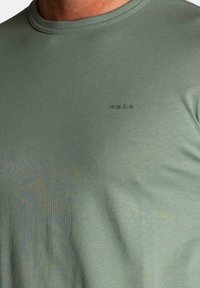 Olijfgroene crew neck t-shirt van een zachte, gladde stof met een subtiele textuur; heeft een kleine donkere logo op de borst.