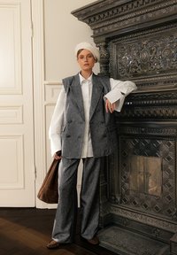 Siva volna brezrokavnik čez belo srajco, v paru s sivimi hlačami. Obleka vključuje mehak kremni baret in rjavto torbo.