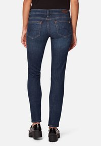 Vaqueros skinny azul oscuro con una textura suave, que presentan una cintura de altura media, bolsillos traseros y discretos acentos de costura. Dobladillo plano en el tobillo.