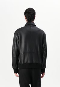 Black leather jacket with a relaxed fit, ribbed hem, and subtle logo detail near the collar. Smooth texture and minimalist design.