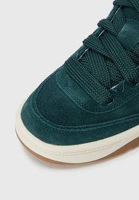 Baskets en daim vert avec tige texturée, bout rond et semelle en caoutchouc crème. Comprend des lacets tissés et des détails de couture renforcés.