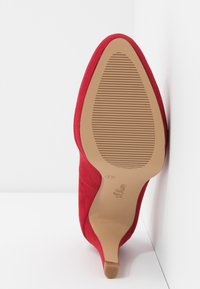 Chaussure en daim rouge à talon haut inclinée vers le haut, montrant une semelle beige avec une adhérence texturée et un petit talon, taille 37 indiquée sur la semelle.