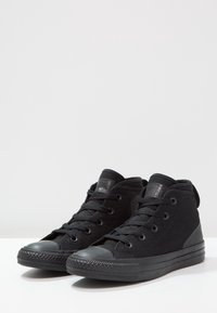 Czarne wysokie trampki z teksturowanego płótna, z czarnym gumowym noskiem i podeszwą, z okrągłymi oczkami i czarnym sznurowaniem.