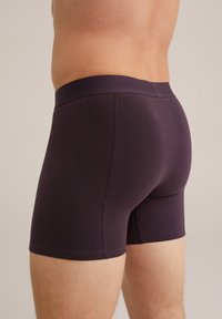 Boxeri din bumbac cu o nuanță violet închis, cu o textură netedă, având o talie lată și un design ajustat, prezentați din lateral.