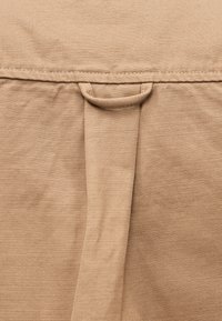 Μπεζ βαμβακερό ύφασμα με υφή στην επιφάνεια και λεπτομέρεια με θηλιά. Η ραφή είναι ορατή στην πάνω άκρη.