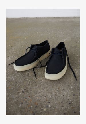 Schwarze Lederschuhe mit glatter Textur, runder Form, weißen Gummisohlen und flachen schwarzen Schnürsenkeln. Minimalistisches Design mit sichtbaren Nähten.