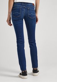 Mörkblå tight jeans med en slät yta, med två bakfickor som har ett sicksacksytt mönster och en brun läderlapp vid midjan.